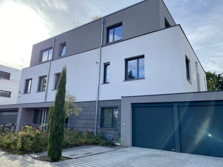 Modern multi-story residential house with white and dark gray facade, dark blue garage doors, and manicured landscape