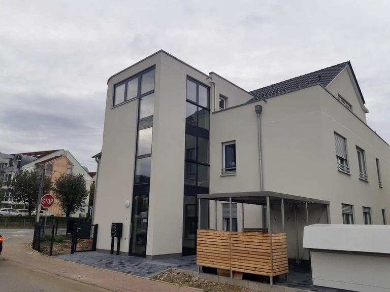 Modern multi-story residential building with white and dark gray exterior, wooden deck entrance, and contemporary architectural design