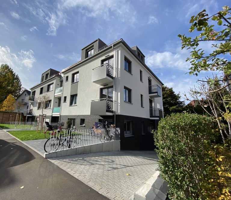 Modern white residential apartment building with mansard roof, bicycle parking, and manicured landscaping