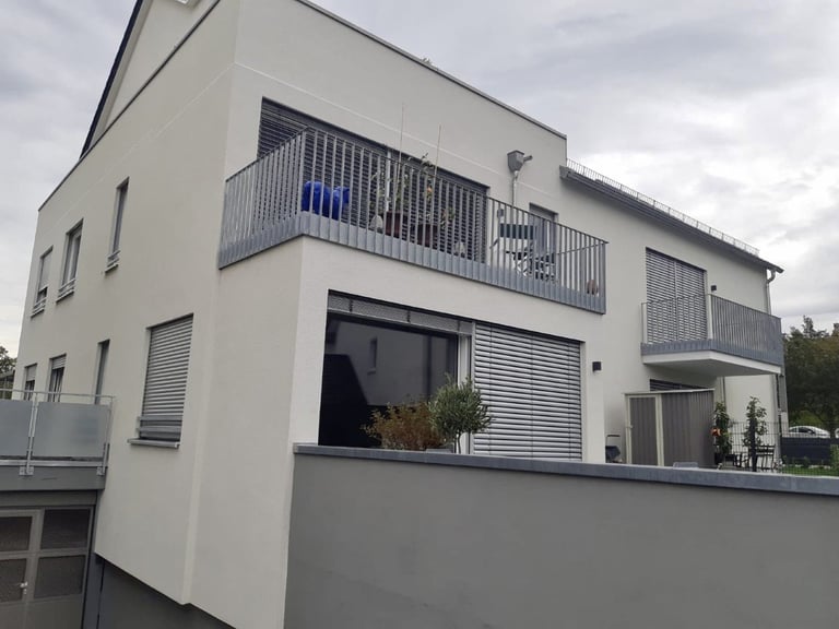 Modern two-story white residential building with metal railings and shuttered windows under cloudy sky