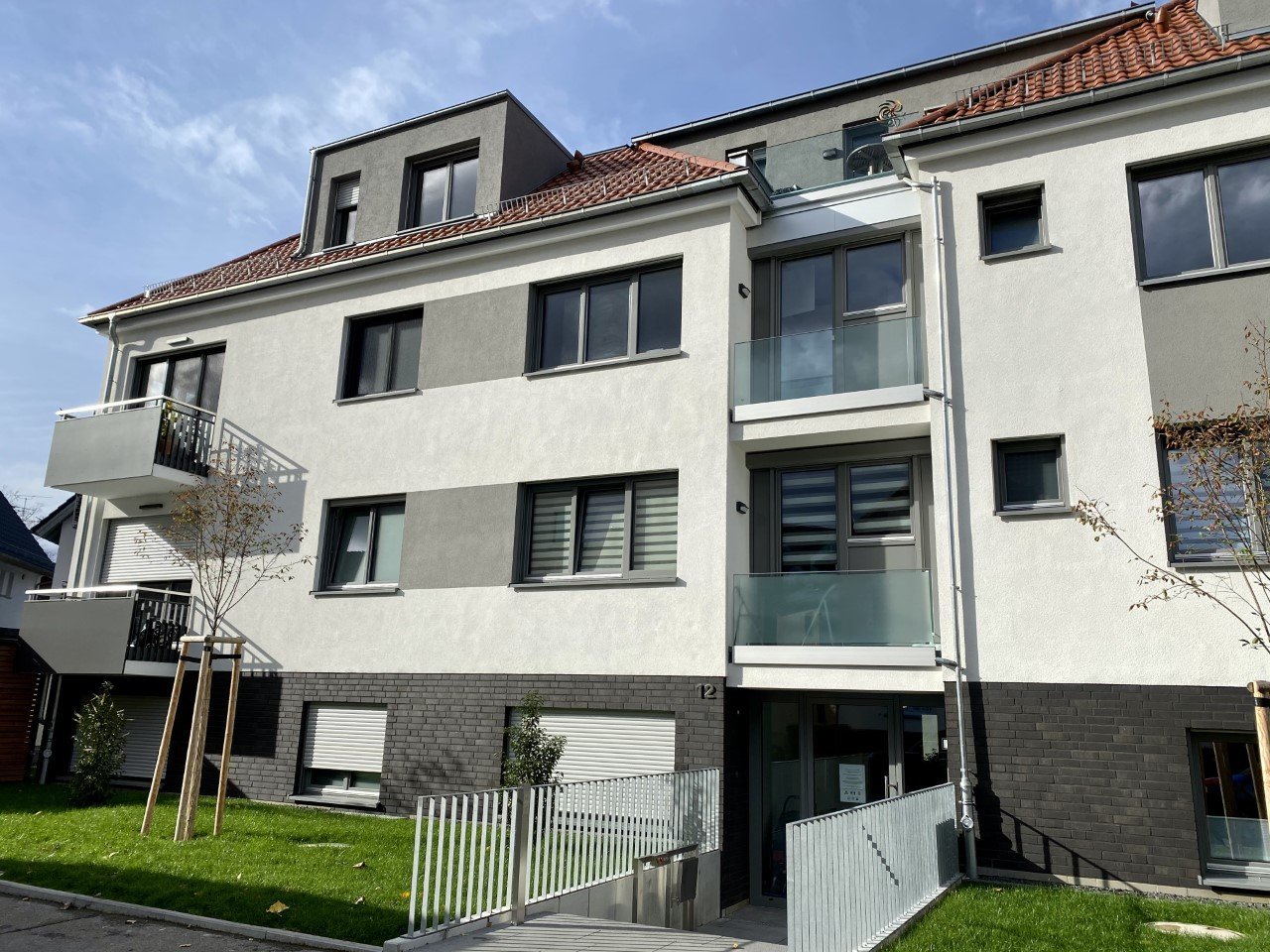 Modern multi-story residential building with cream and dark brick facade, large windows, and metal balconies